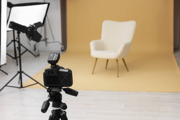 Camera on tripod, armchair and professional lighting equipment in modern photo studio, space for text - Fotó, kép