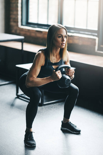 Strength is earned. a young woman working out with a kettle bell in a gym - Foto, Bild