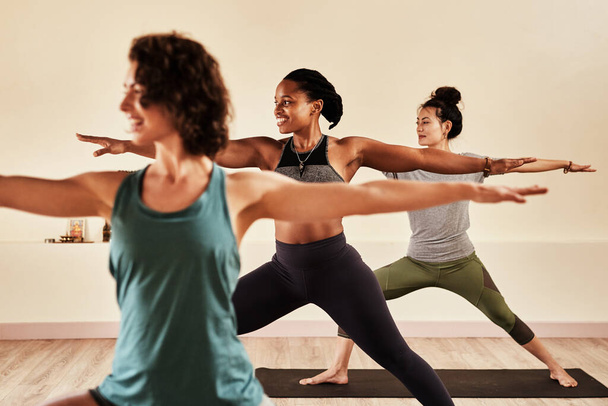 Esteja em total equilíbrio com o seu ser. um grupo de homens e mulheres jovens praticando a pose guerreira durante uma sessão de ioga - Foto, Imagem
