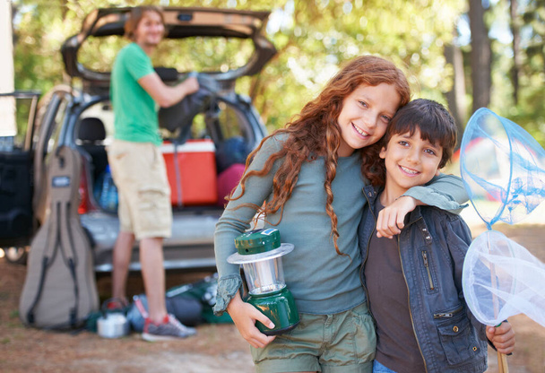 Happy siblings, portrait and hug for camping holiday, road trip or family vacation together in nature. Sister hugging brother with smile and lantern for camp adventure, travel or getaway in forest. - Photo, Image