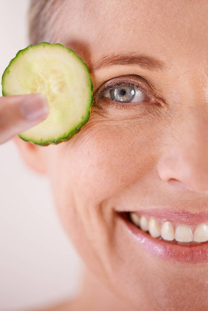 Seeing the world with fresh eyes. Studio shot of a beautiful mature woman posing with a slice of cucumber - Фото, зображення