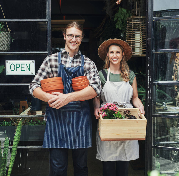 Další den, další výprodej. Stříhaný portrét dvou mladých majitelů podniků, stojících společně u vchodu své květinářství a držících v ruce květináče - Fotografie, Obrázek