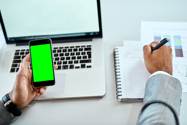 Organize your workday the smart way. Closeup shot of an unrecognizable businessman writing notes while using a cellphone with a green screen in an office - Foto, imagen