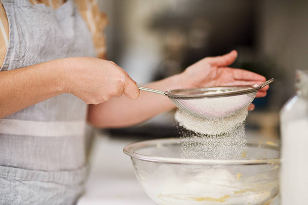 Asegúrate de tamizar la harina. una mujer tamizando harina en un tazón de vidrio - Foto, imagen