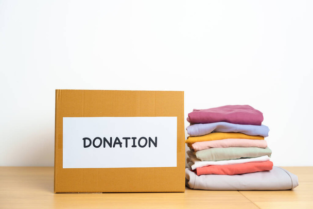 Concepto de Donación, Caridad, Voluntariado, Donación y Entrega. Ropa con caja de donaciones en casa u oficina para apoyar y ayudar a las personas pobres, refugiadas y sin hogar. Copiar espacio para texto - Foto, imagen