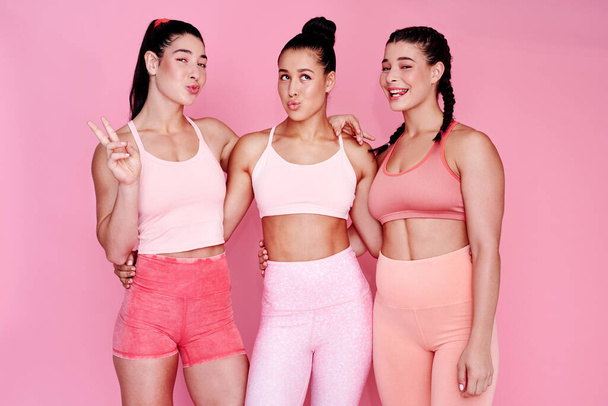 Sportowy z odrobiną pyskowania. Studio portret grupy sportowych młodych kobiet robi twarze stojąc razem na różowym tle - Zdjęcie, obraz