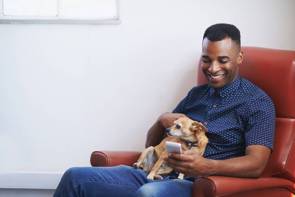 Communication and companionship. A handsome young man using his cellphone with his dog on his lap - Photo, Image