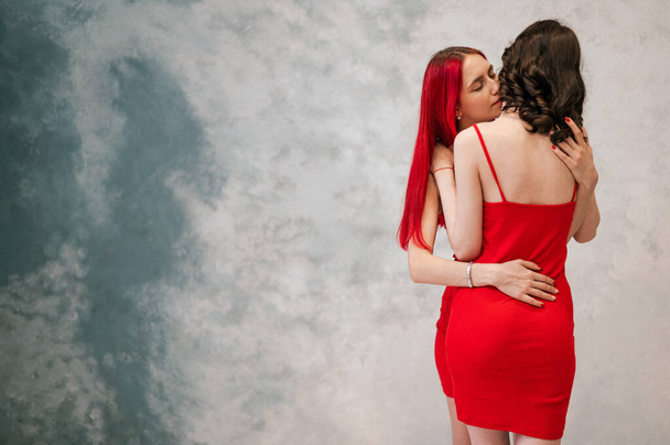 A close-up portrait of two tenderly embracing women dressed in identical red dresses. Lesbian intimacy - Foto, imagen