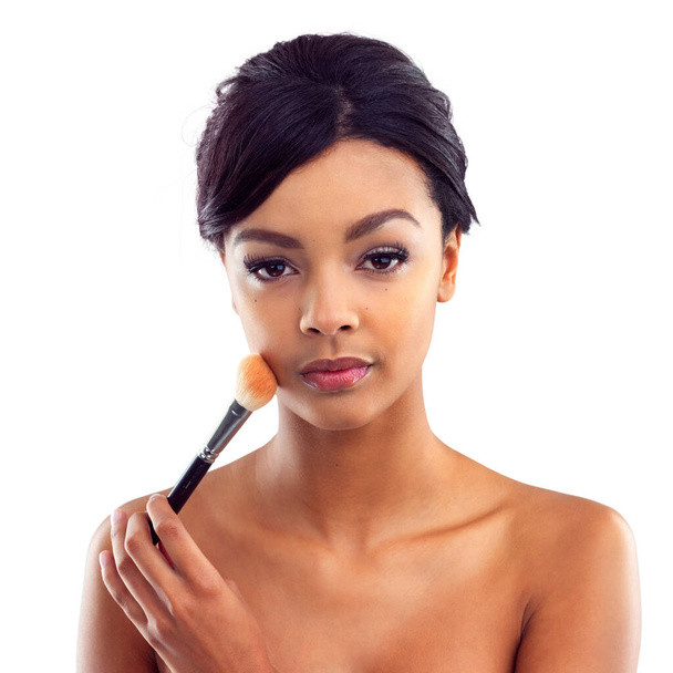 Enhancing her natural beauty with a touch of blush. Studio portrait of an attractive young woman holding a makeup brush to her face - Foto, imagen