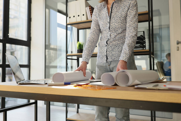 Close-up of designer standing near work desk with rolls of paper. Architect working with new projects - 写真・画像