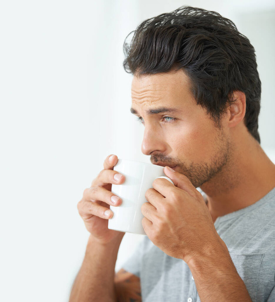 Проснувшись утром, мужчина пьет кофе из кружки в своем доме в одиночестве на выходных, чтобы расслабиться. Лицо, мышление и кофеин с красивым молодым мужчиной-моделью, наслаждающимся свежим напитком в своем доме. - Фото, изображение