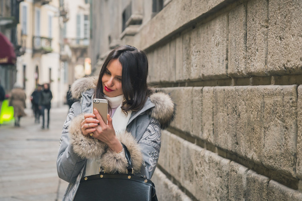 Beautiful young brunette texting in the city streets - 写真・画像