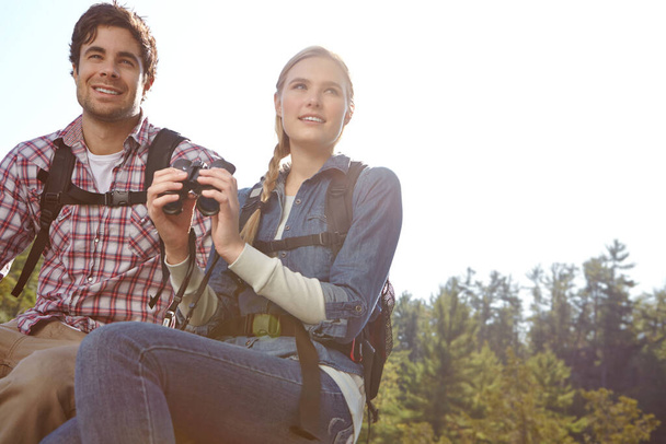 Tómese un momento para apreciar la vista. Una pareja joven en la cima de una montaña mientras sostiene sus prismáticos - Foto, Imagen