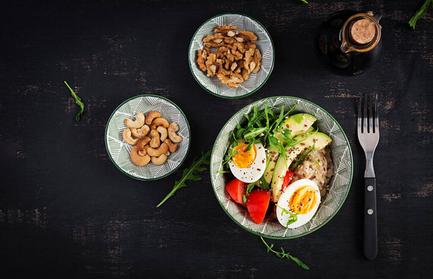 Овсяная каша на завтрак с вареными яйцами, авокадо, помидорами и зелеными травами. Здоровое сбалансированное питание. Вид сверху, плоский - Фото, изображение