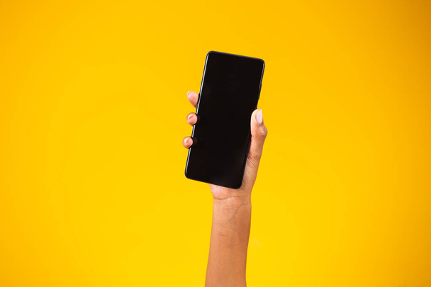 hand holding black smartphone isolated on yellow background - Photo, image