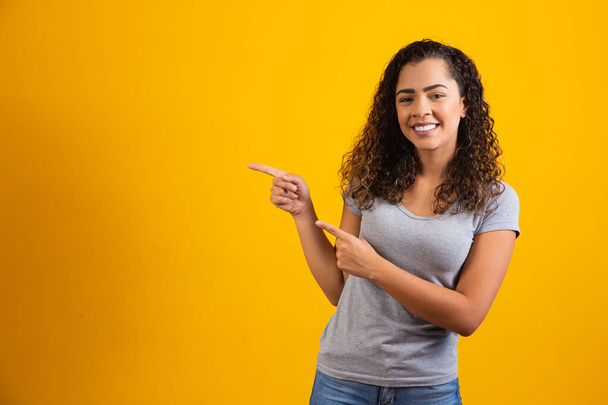 Afro woman pointing in yellow background with space for the text - Photo, Image
