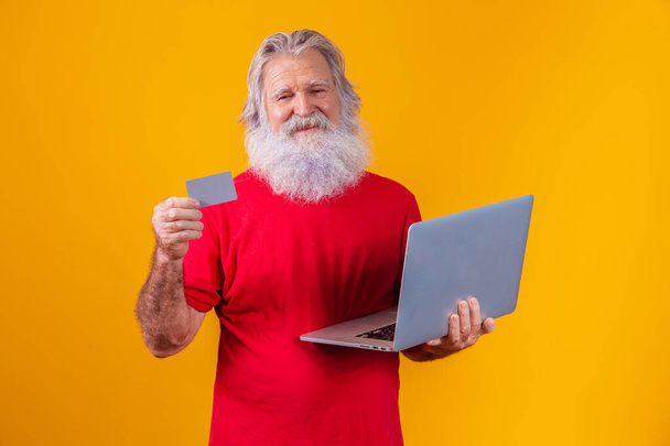 Elderly man holding laptop computer and bank credit card. Online shopping transaction. Mobile banking cashless method. - Photo, image