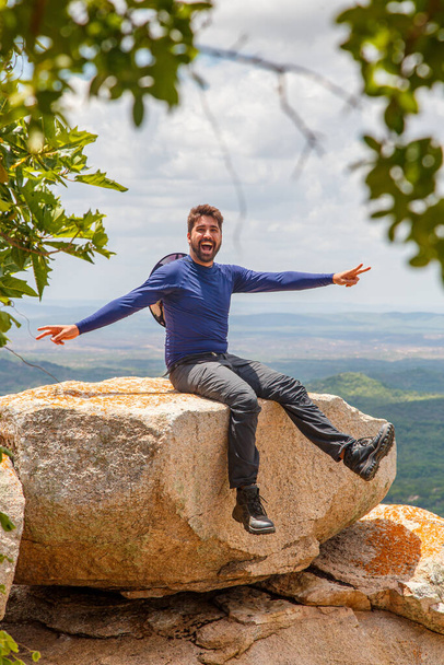 man with open arms sitting on the rock on a mountain. Adventure and victory concept - Fotografie, Obrázek