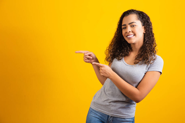 Afro woman pointing in yellow background with space for the text - Фото, изображение