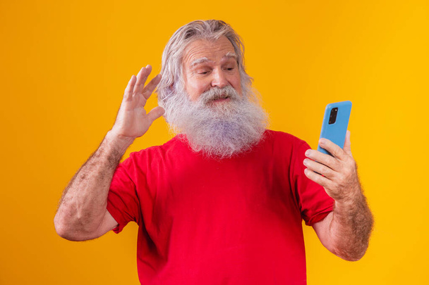 Homme âgé joyeux tenant un smartphone, ayant un appel vidéo en ligne, bavardant avec des enfants adultes, communiquant avec un ami à distance, technologie moderne de génération plus ancienne concept convivial confortable. - Photo, image