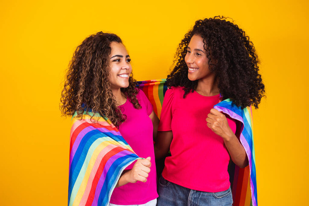 Couple lesbian woman with gay pride flag in yellow background - Foto, imagen