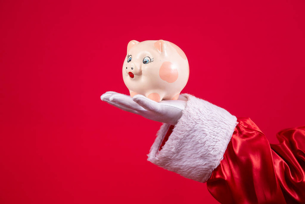 Close-up of Santa's gloved hand holding a piggy bank. - Foto, afbeelding