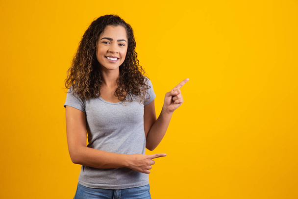 Afro woman pointing in yellow background with space for the text - Фото, изображение