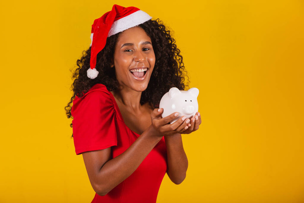 Beautiful young woman taking up the savings from a piggy bank to buy the christmas presents. Young woman with a piggy bank - Foto, afbeelding