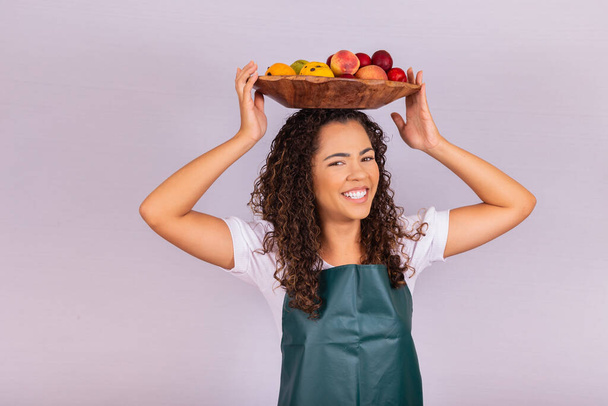 smiling afro girl with fruit basket on her head smiling at camera - Фото, изображение