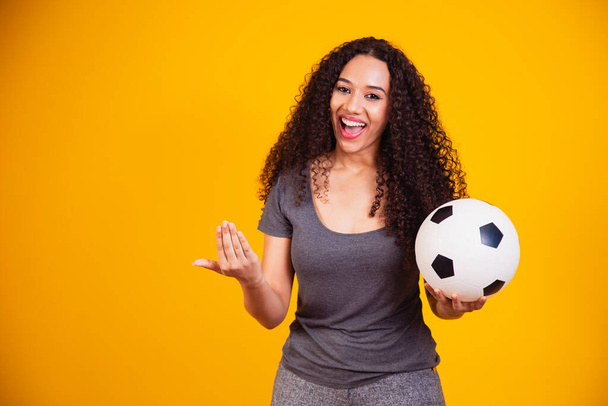 Young African American woman isolated on yellow background with soccer ball - Фото, изображение