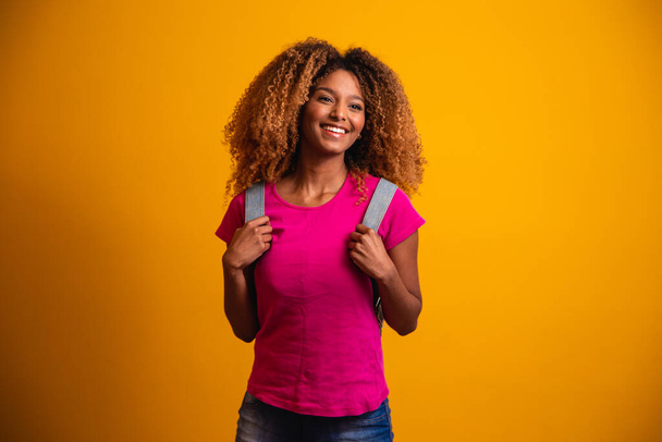 young afro with backpack on his back on yellow background. young student smiling - Foto, Imagem