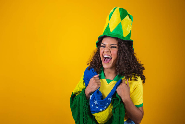 Brazil supporter. Brazilian curly hair woman fan celebrating on soccer, football match on yellow background. Brazil colors. - Foto, afbeelding