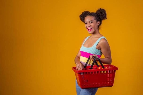 Smiling afro woman holding empty shopping basket looking at camera smiling - Fotoğraf, Görsel