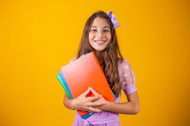 Beautiful smiling girl holding books going to school. close up portrait, isolated yellow background, childhood. child hugging notebooks. lifestyle, interest, hobby, free time, free time - Foto, Imagen