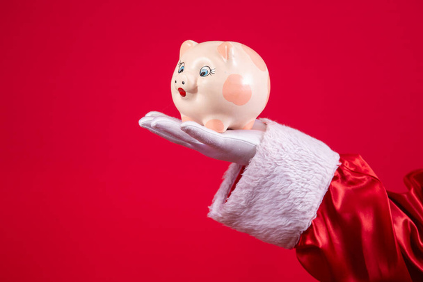 Close-up of Santa's gloved hand holding a piggy bank. - 写真・画像