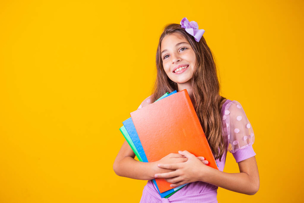 Beautiful smiling girl holding books going to school. close up portrait, isolated yellow background, childhood. child hugging notebooks. lifestyle, interest, hobby, free time, free time - Photo, image