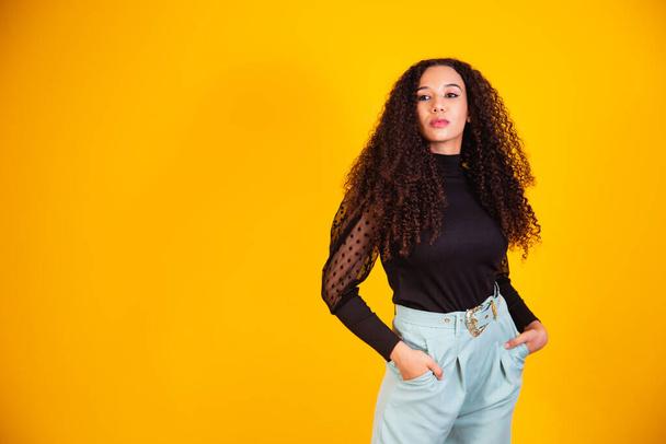 Beauty portrait of a Brazilian woman with afro hairstyle and glamour makeup. Latin woman. Mixed race. Curly hair. Hair style. Yellow background - Foto, imagen
