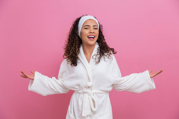 beautiful afro girl dressed in white bathrobe and sash on pink background with space for text. health and care concept - Fotó, kép