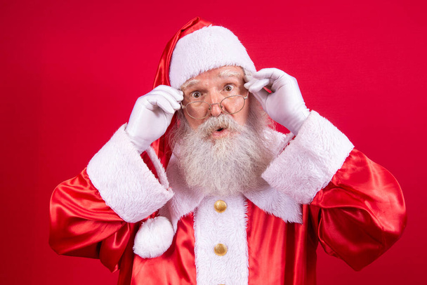 Santa Claus looking at the camera. Christmas is coming. Merry Christmas. Santa is watching. Holding his glasses. - Foto, imagen