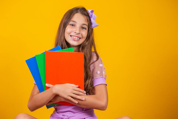 Krásná usměvavá dívka s knihami ve škole. zavřít portrét, izolované žluté pozadí, dětství. dítě objímající zápisníky. životní styl, zájem, koníček, volný čas, volný čas - Fotografie, Obrázek