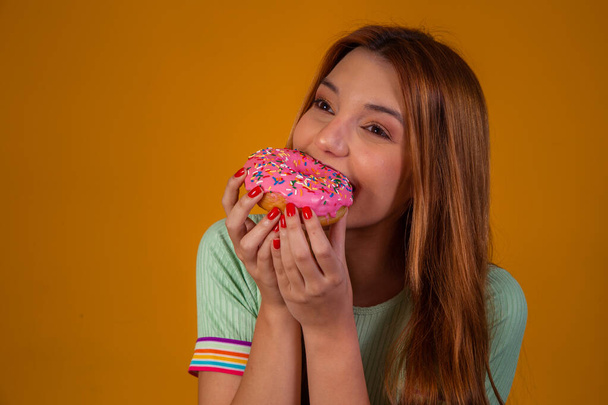 girl eating pink donuts on yellow background. - Фото, зображення