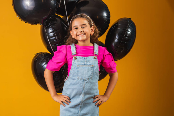 smiling little girl with black balloons on black friday. low price festival - Foto, afbeelding