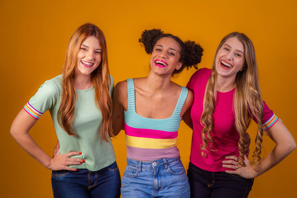 Sarı arka plandaki mutlu kız arkadaşlar çeşitlilik gösteriyor. Kızıl saçlı, afro saçlı ve sarı arka planda sarışın. çeşitlilik kavramı - Fotoğraf, Görsel