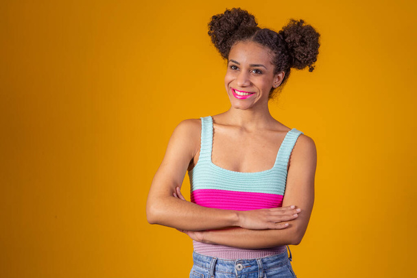 Afro young woman with arms crossed on yellow background with bun in her hair. - Valokuva, kuva