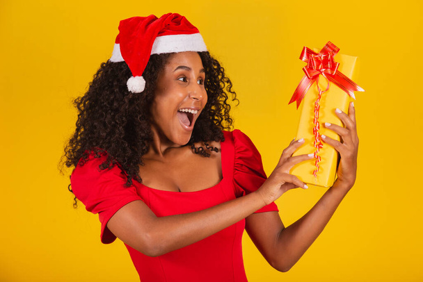 Young afro girl holding an expressive Christmas present. - Foto, Imagen
