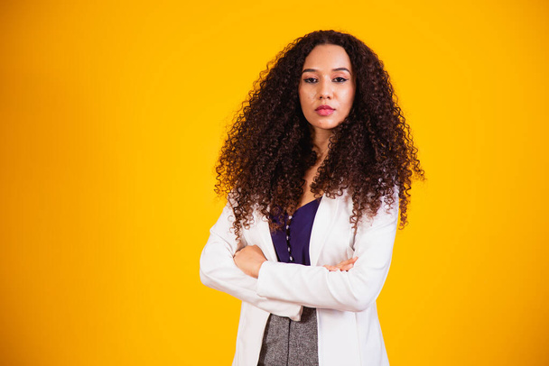 Young afro business woman with arms crossed on yellow background. - Foto, Imagen