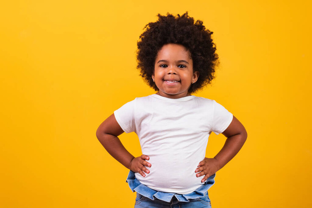 Концепция детства и людей - счастливая маленькая африканская американская девочка на желтом фоне. Маленькая черная девочка с черными волосами силы улыбается. - Фото, изображение
