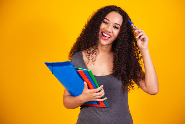 Young African American teenage student in casual clothes holding books isolated on yellow background studio portrait. Education at high school university college concept. mock up copy space - Photo, Image