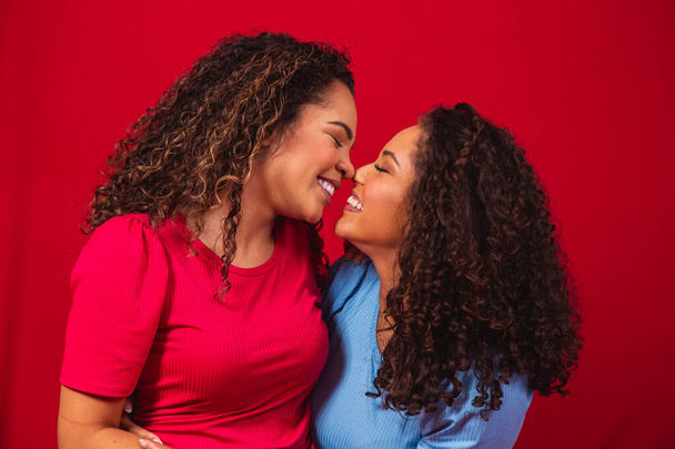 Portrait of young afro women lesbian couple on red background. LGBT concept - Фото, изображение