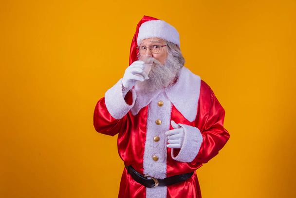 Santa Claus drinking a glass of water on yellow background with space for text. Health and hydration concept - Фото, изображение